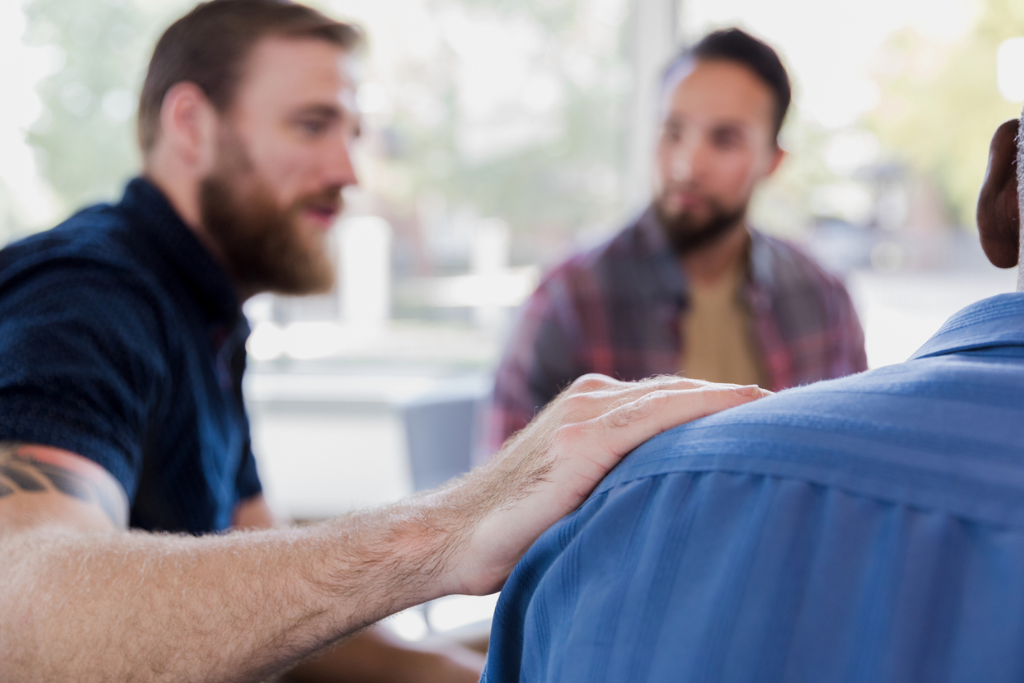 Man’s hand on man’s shoulder during a EVRYMAN group session